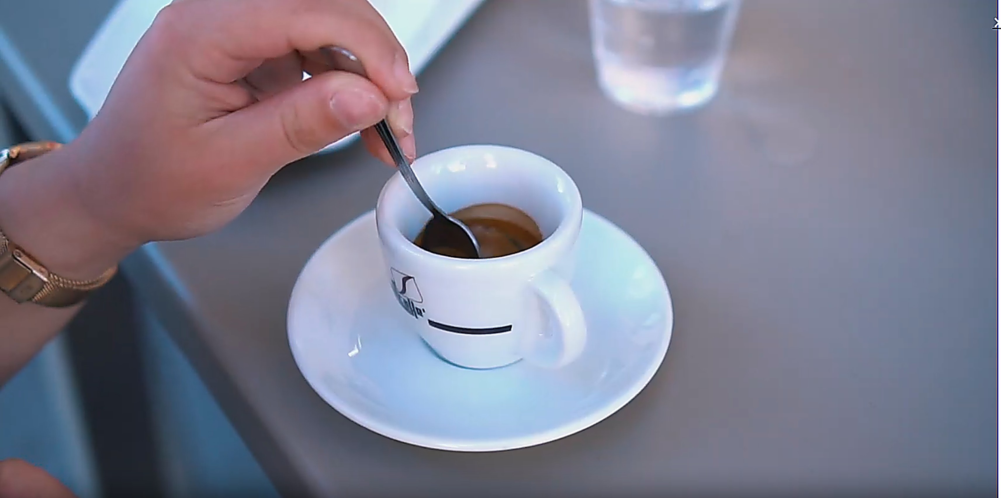 Šálek Bellcaffe se sklenicí vody na stolku italské kavárny